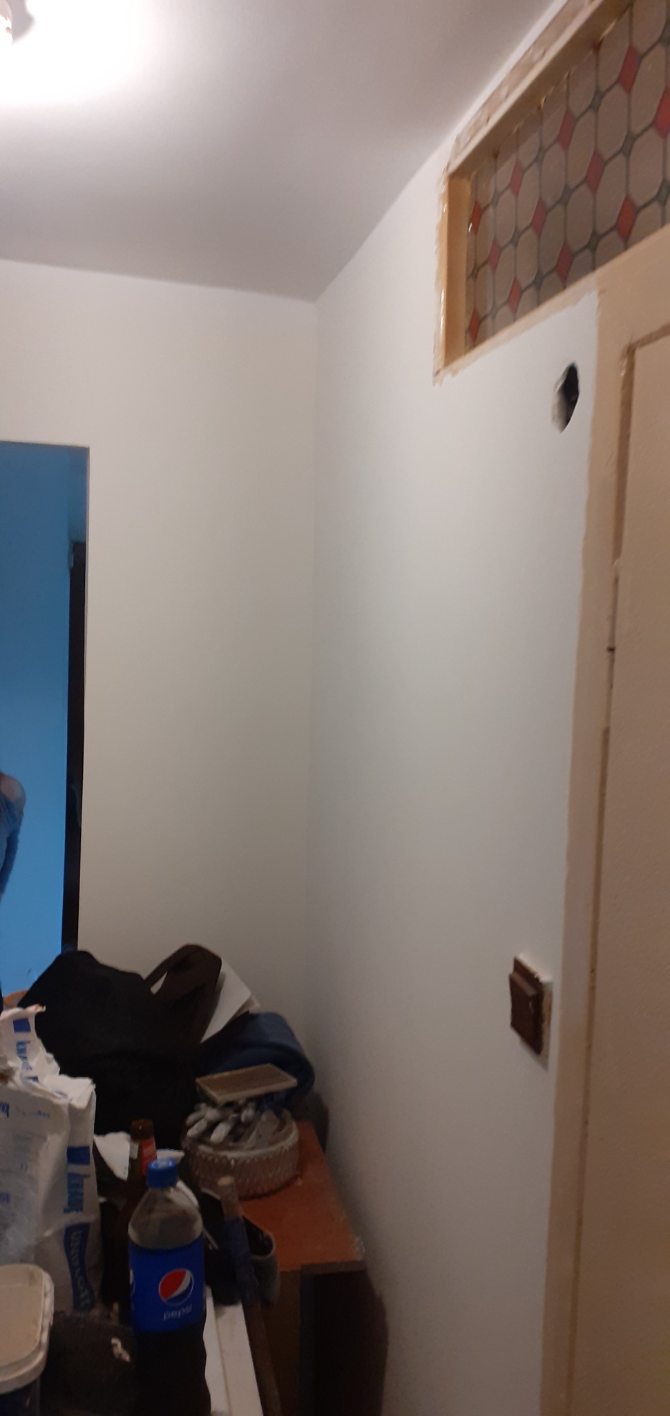 Świeżo pomalowane białe ściany w pokoju podczas remontu, widoczna dziura w ścianie, gniazdko elektryczne, fragment drzwi i dekoracyjny element nad nimi, na pierwszym planie materiały budowlane...