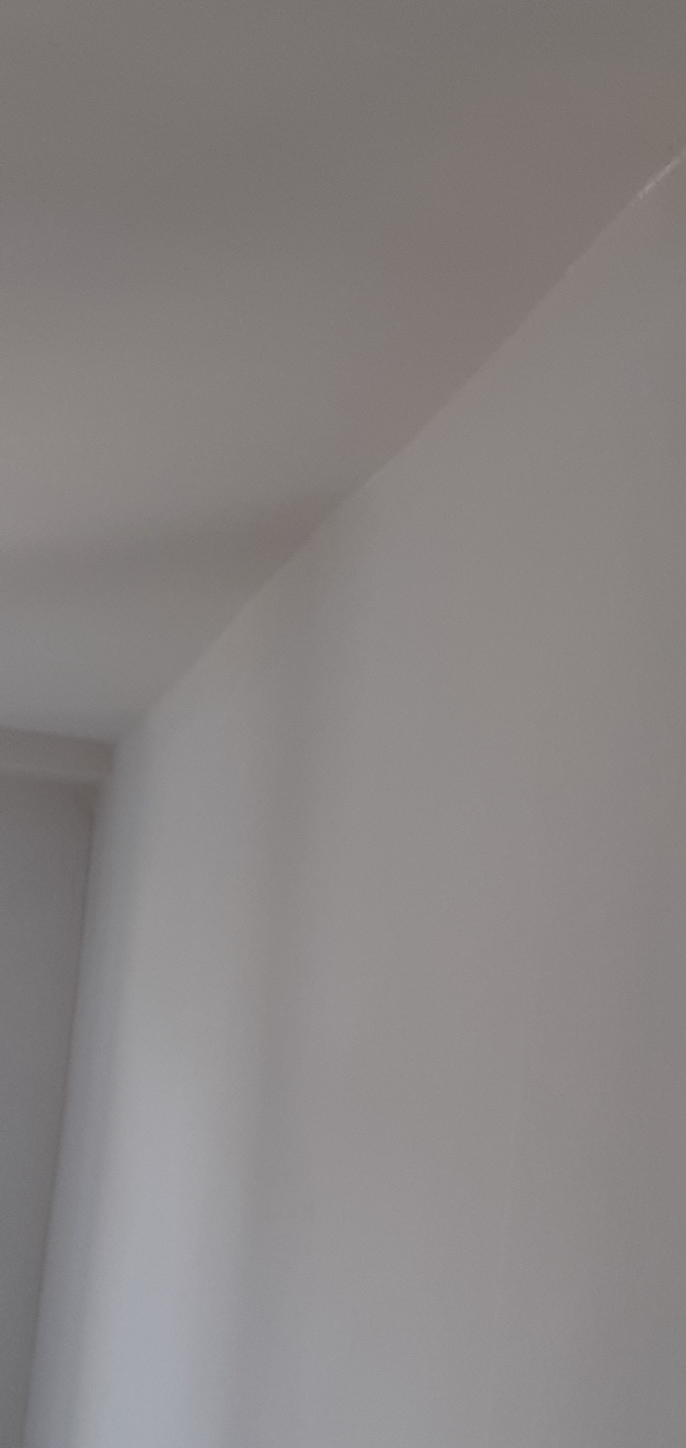 Świeżo pomalowany róg pokoju z widocznym łączeniem ściany i sufitu, wykończony na gładko, w jasnym odcieniu bieli.