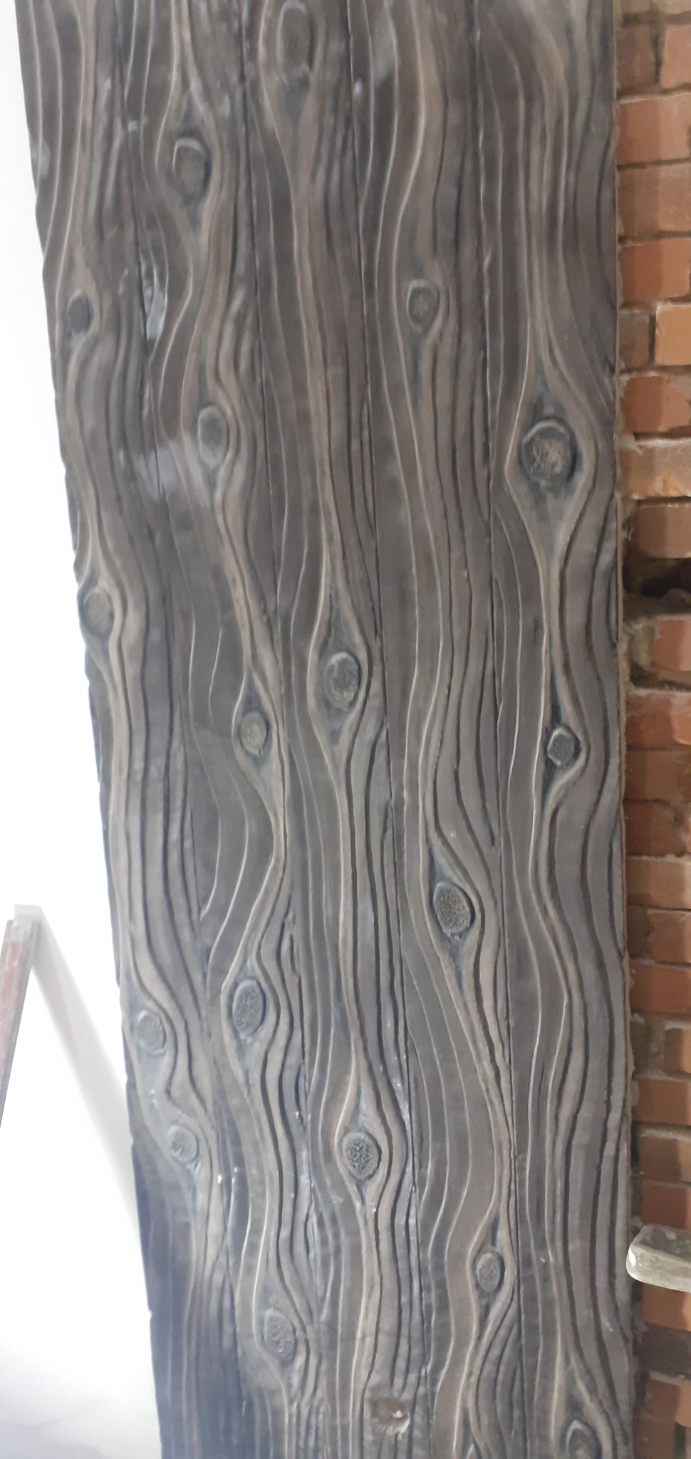 Panel ścienny z fakturą drewna w odcieniach szarości, sąsiadujący z fragmentem ściany z czerwonej cegły.