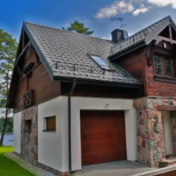 Dwukondygnacyjny dom z brązowego drewna z garażem i kamienną elewacją, grafitowy dach z oknem połaciowym, na tle zieleni i jeziora.