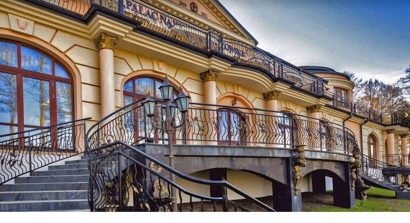 Elewacja dwupiętrowego budynku z kolumnami, balkonami z ozdobnymi balustradami i schodami wejściowymi z kutymi poręczami, w stylu klasycystycznym.