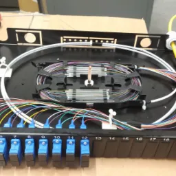 Panel krosowniczy światłowodowy z ponumerowanymi portami, kolorowymi kablami i spiralnie ułożonymi włóknami w czarnej obudowie.