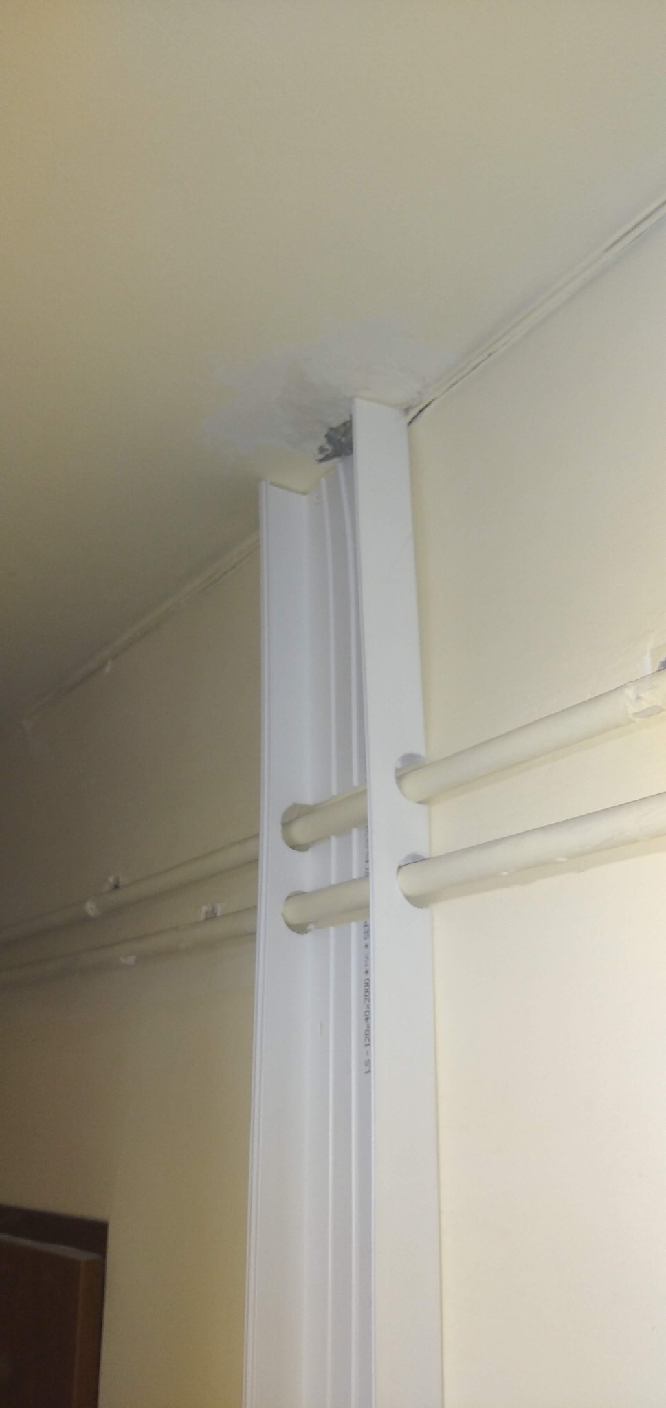 Biała listwa przypodłogowa z otworami na rury centralnego ogrzewania, zamontowana przy ścianie i suficie w pomieszczeniu o kremowych ścianach.