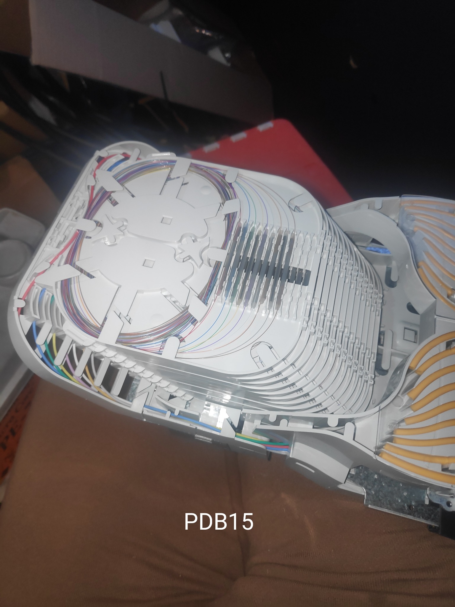 Otwarta, biała skrzynka telekomunikacyjna PDB15 z ułożonymi kolorowymi kablami światłowodowymi wewnątrz.