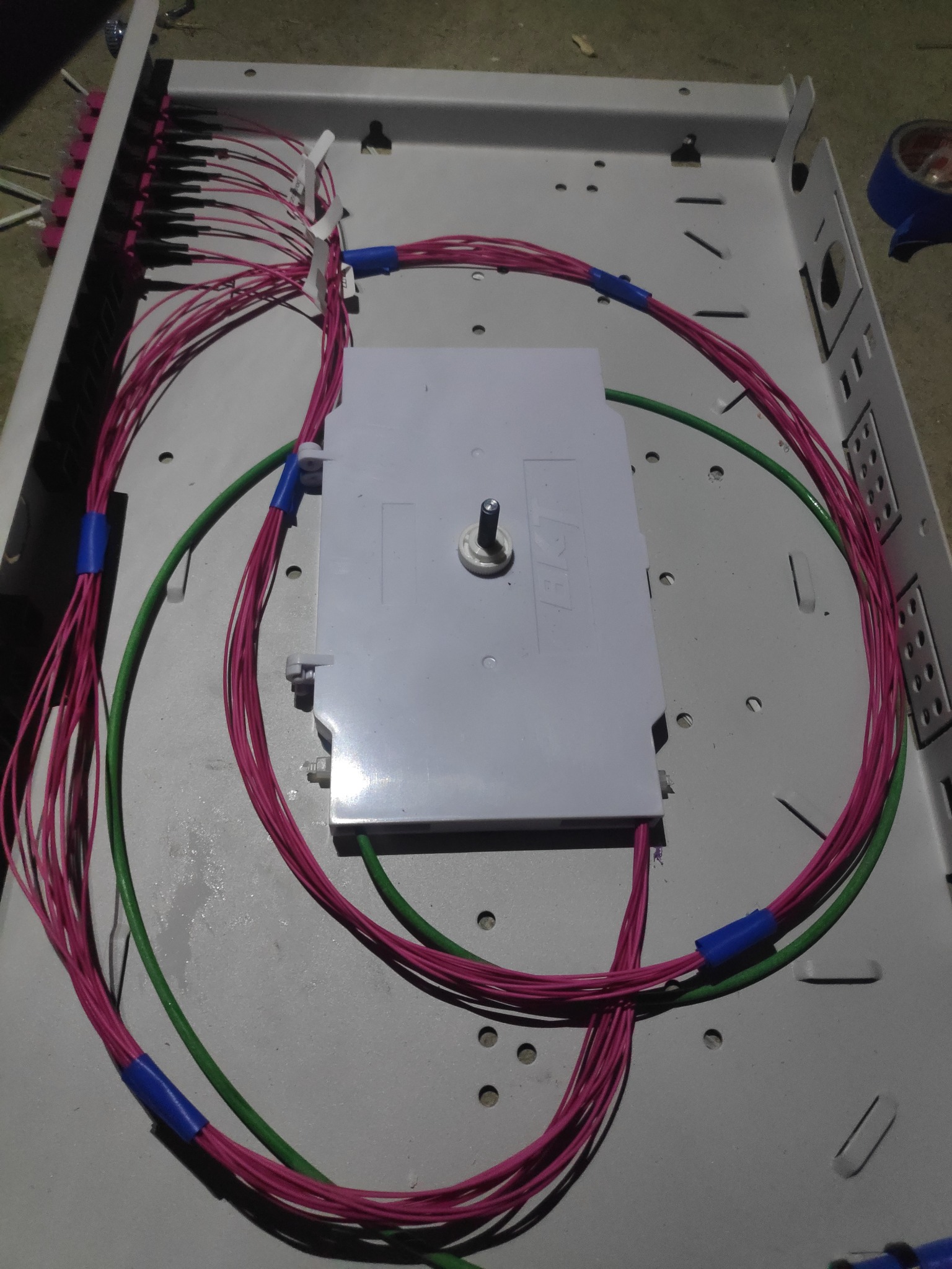 Instalacja światłowodowa: rozdzielnica z podłączonymi kablami światłowodowymi w kolorach różowym i zielonym, zabezpieczonymi niebieską taśmą.