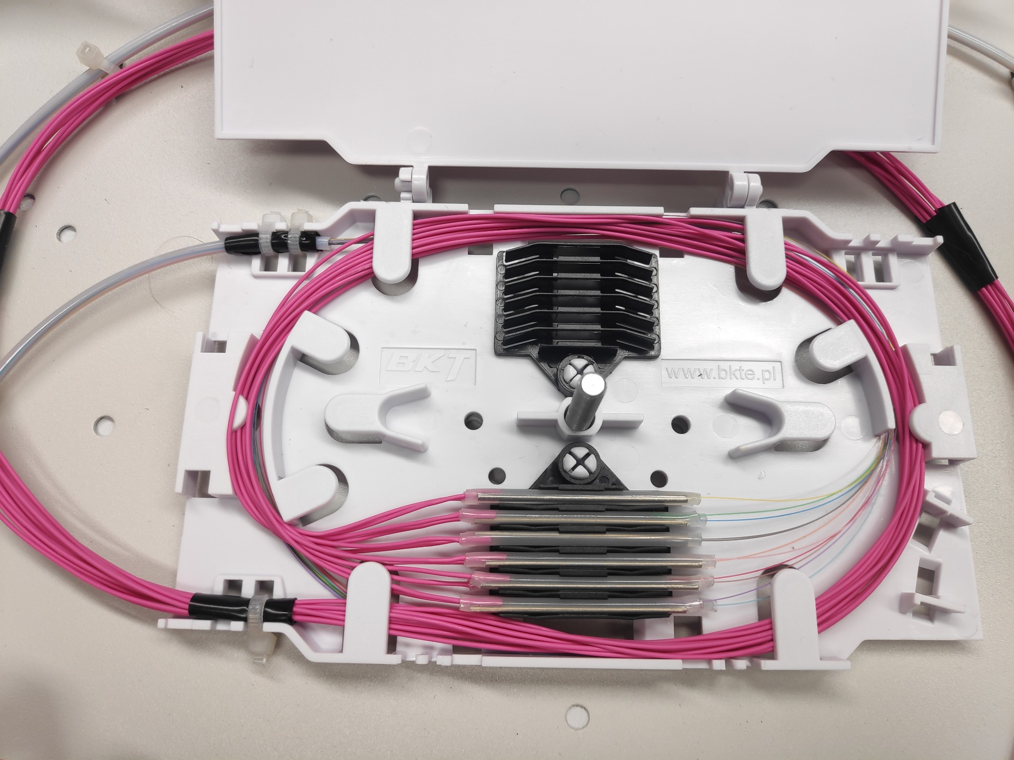 Rozdzielnica światłowodowa z widocznymi włóknami optycznymi w kolorowych osłonkach, ułożonymi wewnątrz białej obudowy z tworzywa sztucznego.