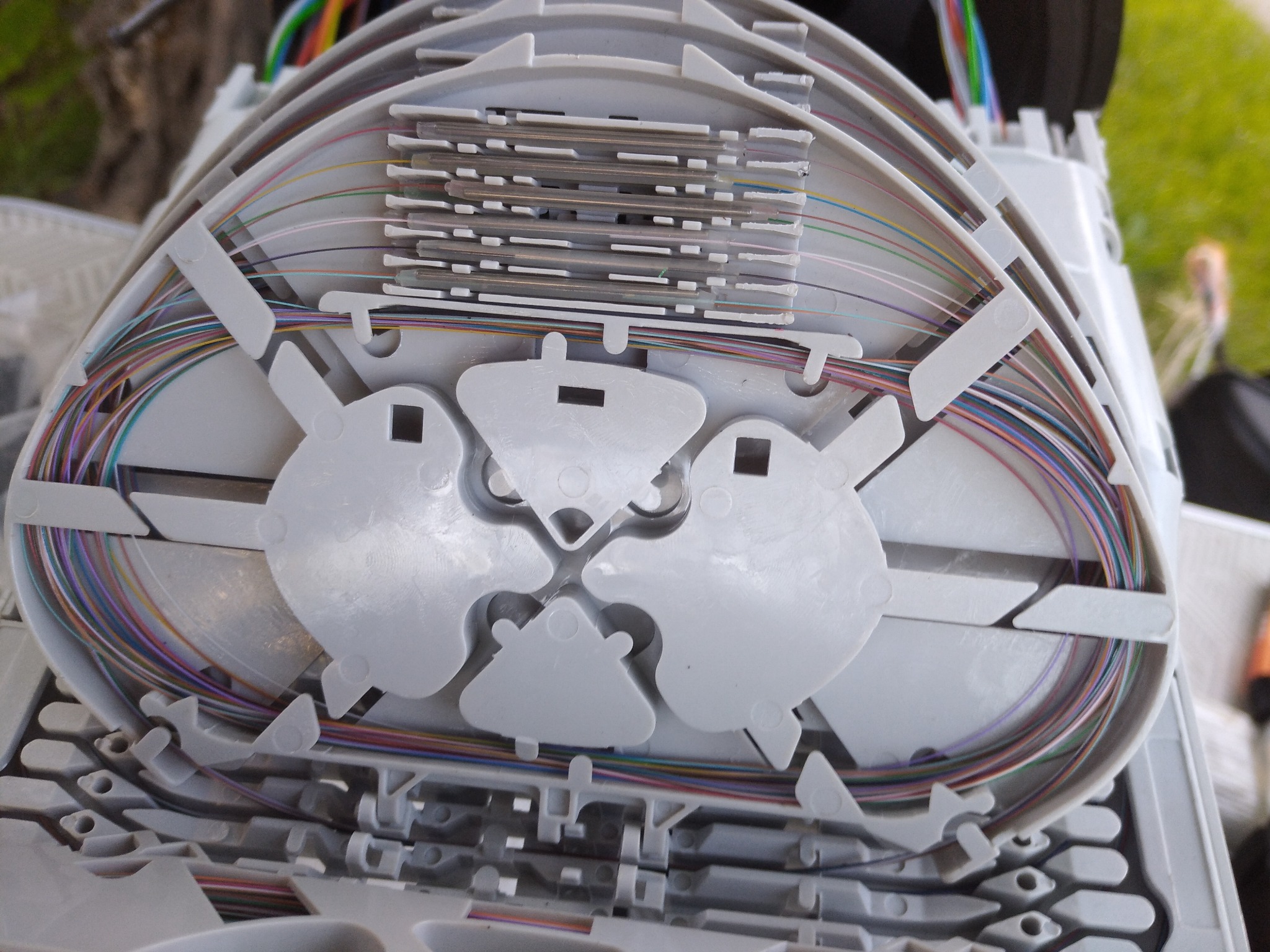 Otwarta, szara puszka telekomunikacyjna z widocznymi, uporządkowanymi światłowodami w różnych kolorach, ułożonymi wewnątrz w okrągłe pętle.