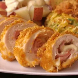 Zapiekane roladki z kurczaka z szynką i serem, podane z sałatką warzywną i ziemniakami.