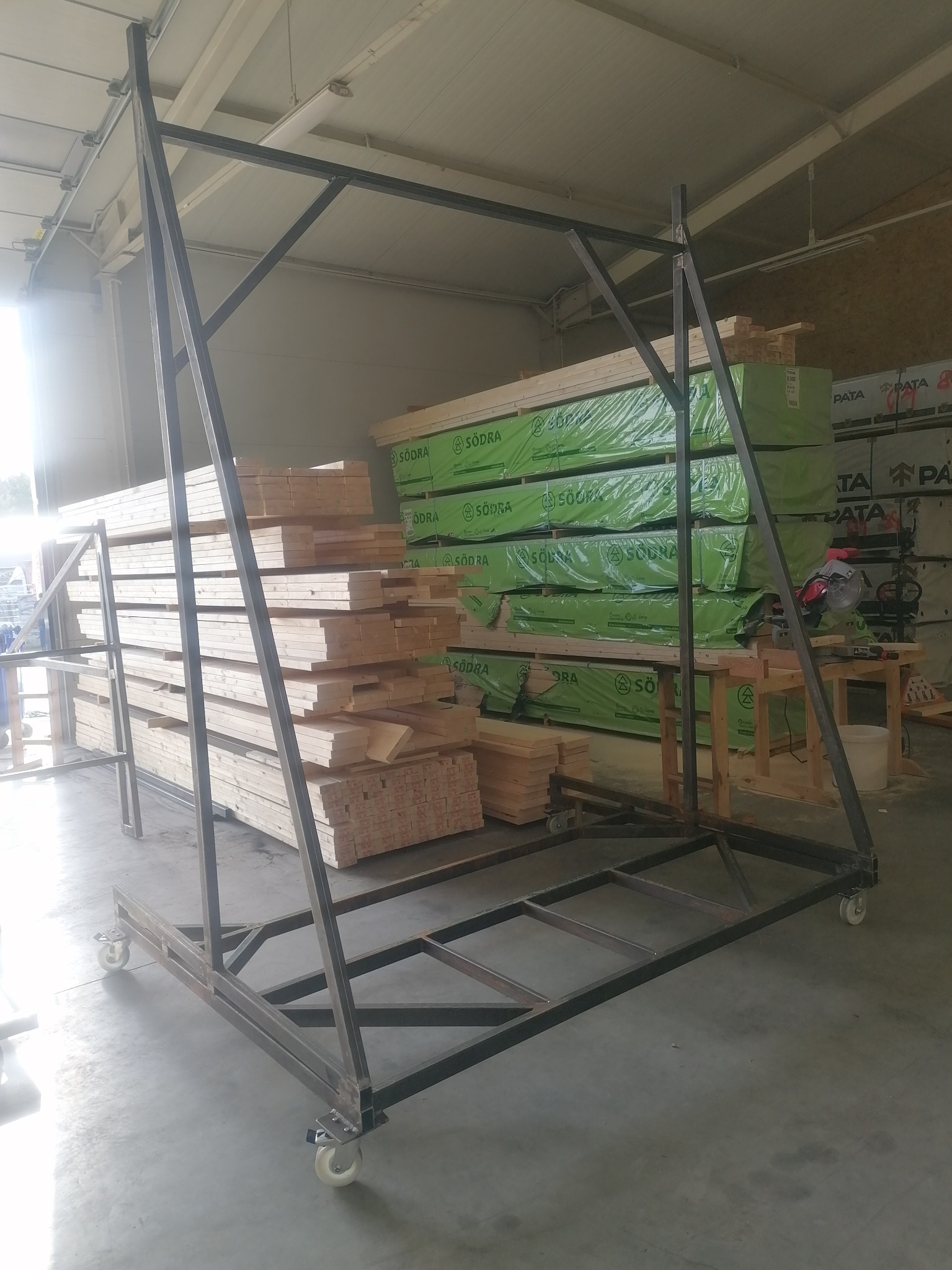 Metalowy wózek transportowy z drewnem na tle magazynu z zapasami drewna Södra