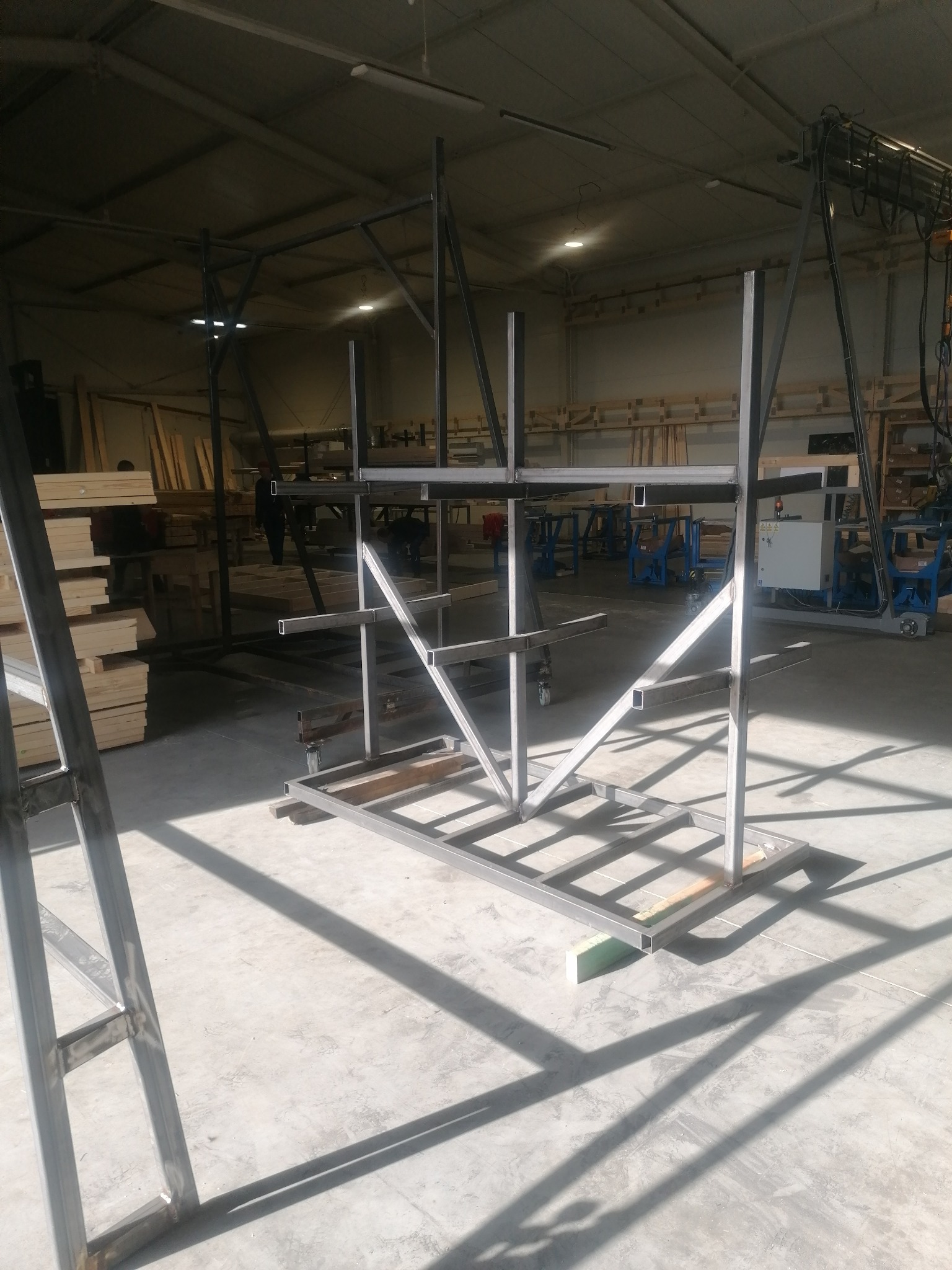 Metalowa konstrukcja regału na kółkach, spawana z profili kwadratowych, w hali produkcyjnej, z widocznymi śladami spawania i surowym wykończeniem.