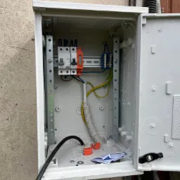 Otwarta skrzynka elektryczna z zamontowanymi bezpiecznikami różnicowoprądowymi Legrand i Simlic, widoczne przewody, listwa zaciskowa, fragment dokumentacji i drobne ścinki wewnątrz obudowy,...