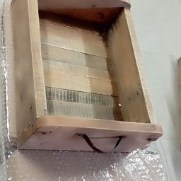 REKWIZYTORNIA KRZYSZTOF HULBÓJ - Surowe drewniane pudełko z uchwytem, wykonane z desek o różnym odcieniu, zabezpieczone folią bąbelkową.