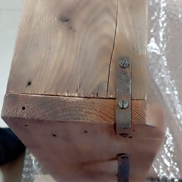 REKWIZYTORNIA KRZYSZTOF HULBÓJ - Fragment surowego, drewnianego blatu z widocznymi sękami, pęknięciami i metalowymi mocowaniami, leżący na folii bąbelkowej.