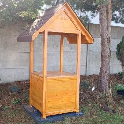 REKWIZYTORNIA KRZYSZTOF HULBÓJ - Drewniana kapliczka ogrodowa z brązowym dachem, widok z przodu na tle zieleni i betonowego ogrodzenia.