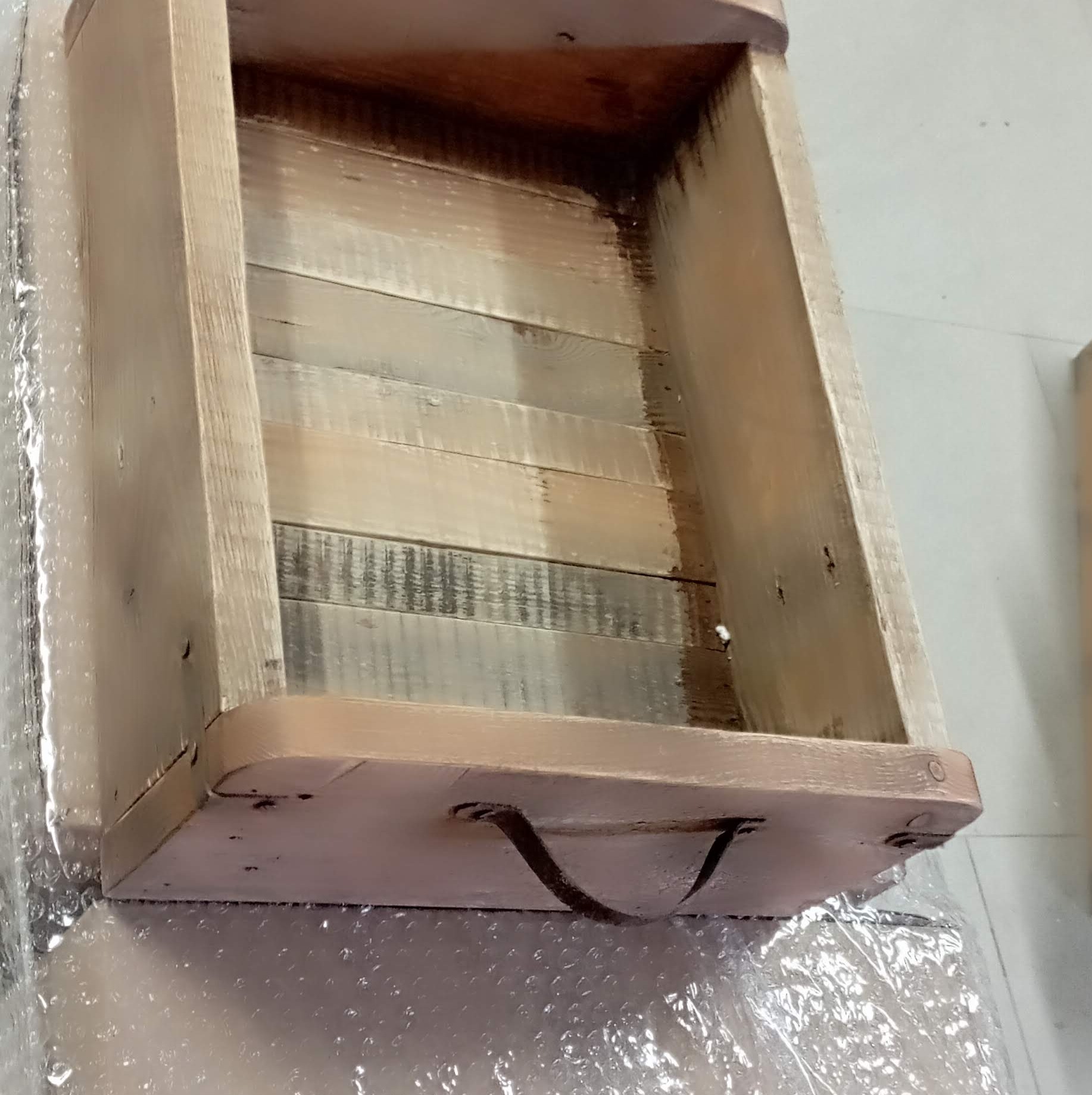 Surowe drewniane pudełko z uchwytem, wykonane z desek o różnym odcieniu, zabezpieczone folią bąbelkową.