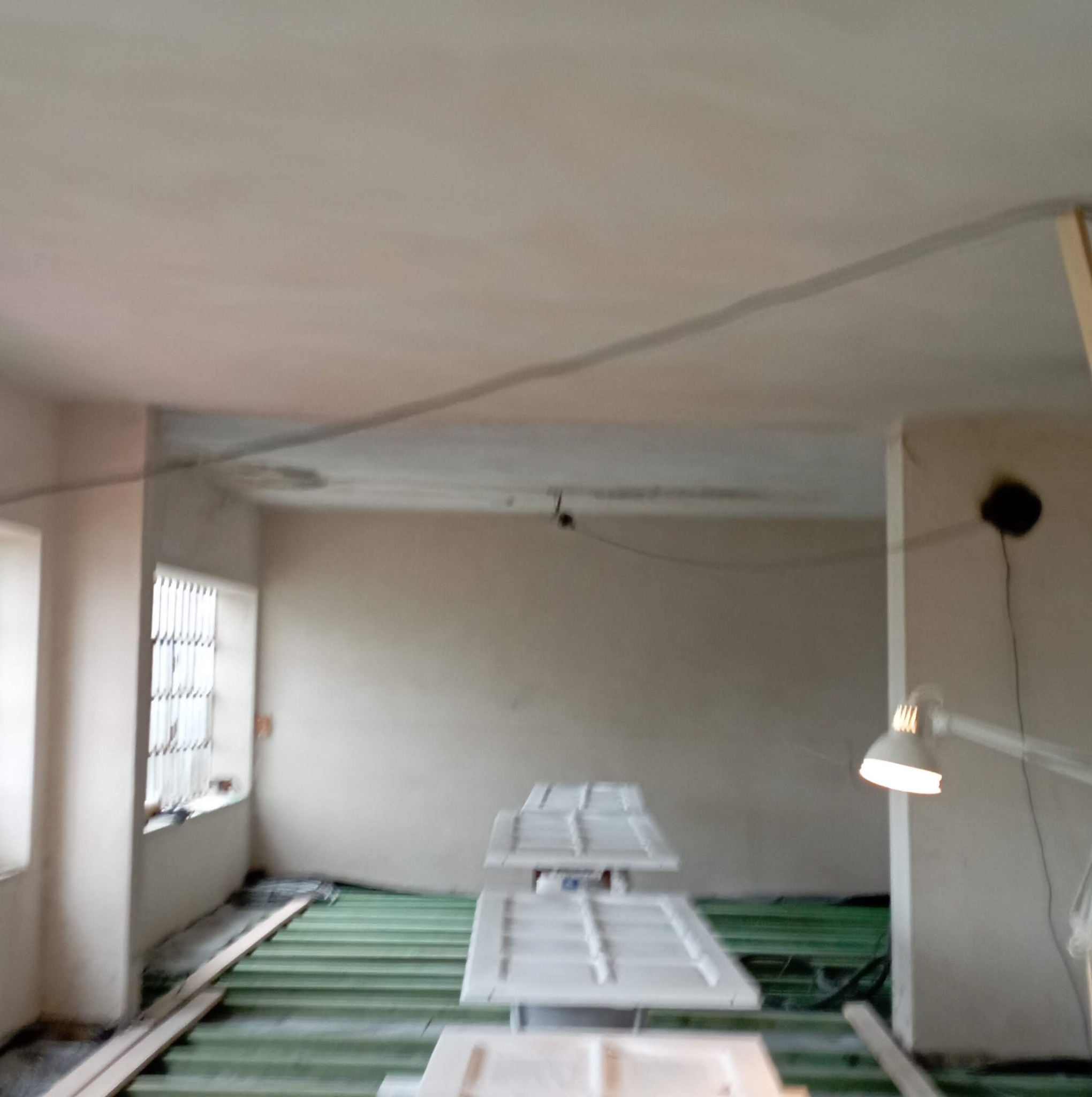 Wnętrze w trakcie remontu z kilkoma białymi drzwiami leżącymi na podłodze, oświetlone lampą.