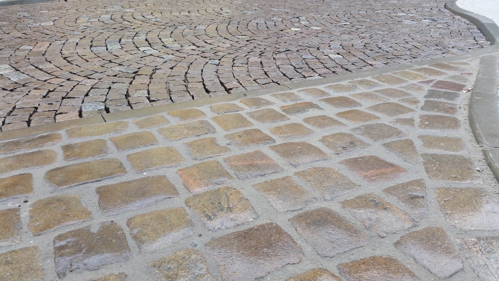 Dwa rodzaje kostki brukowej: regularna i ułożona w okręgi, oddzielone betonowym obrzeżem.