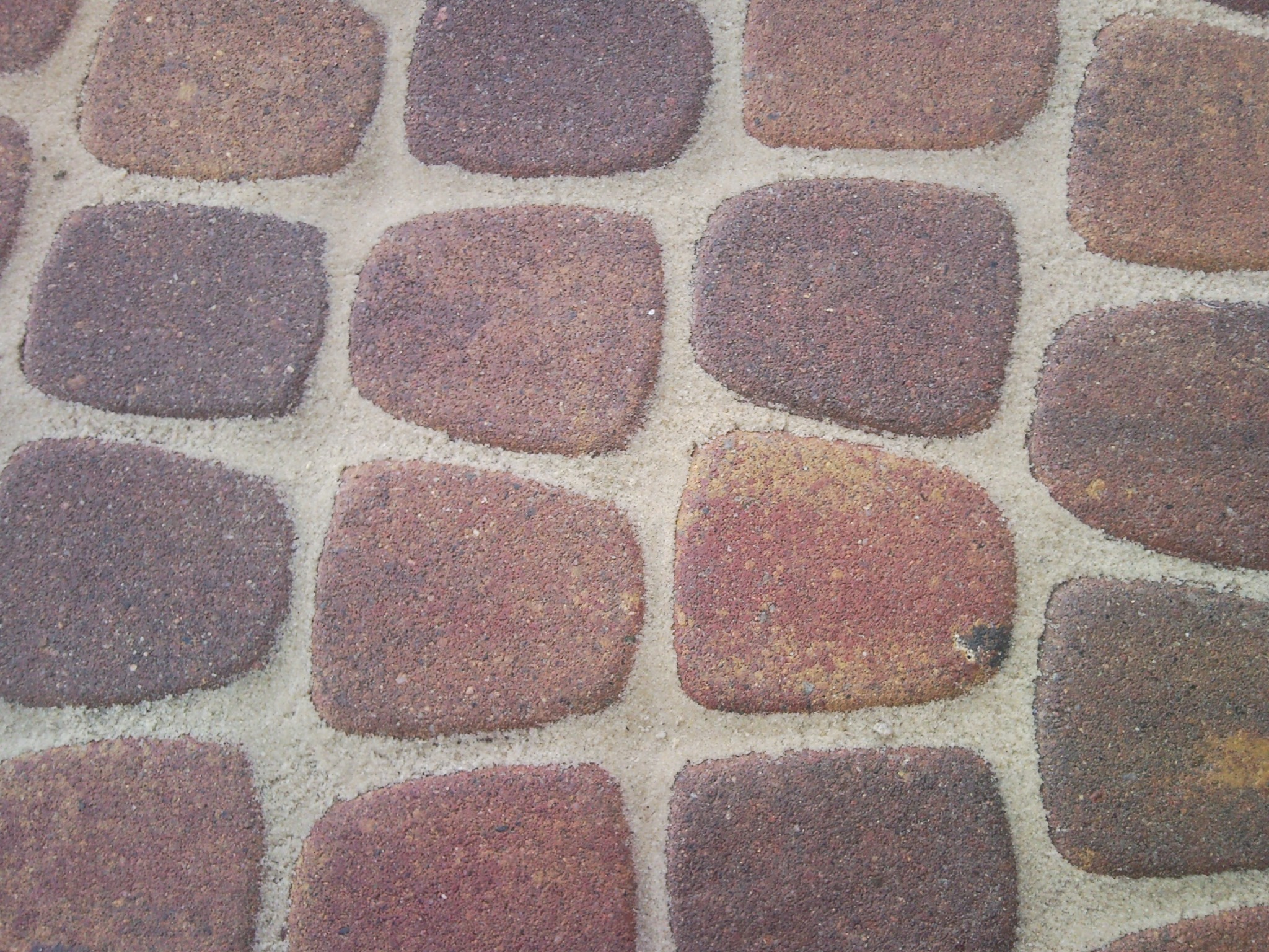 Zbliżenie na nawierzchnię z kostki brukowej w odcieniach brązu, z jasnymi fugami wypełnionymi piaskiem.