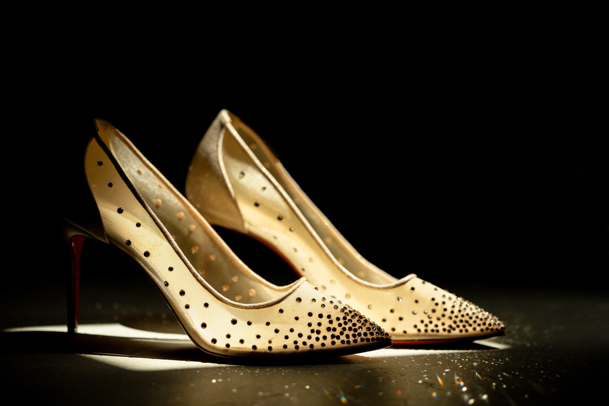 Eleganckie, złote szpilki z siateczki, ozdobione czarnymi kropkami, na czarnym tle, z czerwonymi obcasami, oświetlone punktowo.