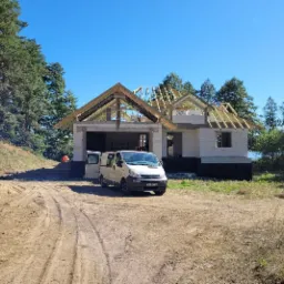 Budowa domu jednorodzinnego w stanie surowym otwartym, widoczny szkielet dachu, biały bus dostawczy zaparkowany obok.