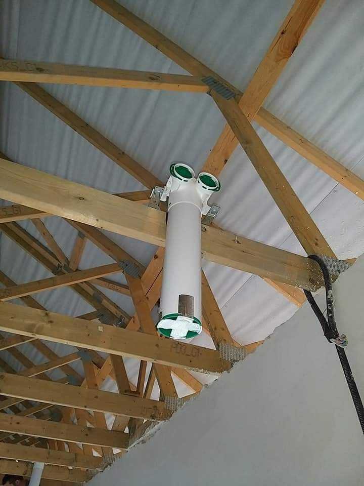 Centralny element instalacji wentylacyjnej z zielonymi detalami, zamontowany pod drewnianą konstrukcją dachu w nowym budynku.