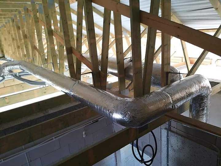 Instalacja kanałów wentylacyjnych w folii aluminiowej w budynku w Gdańsku, widoczne drewniane elementy konstrukcyjne dachu.