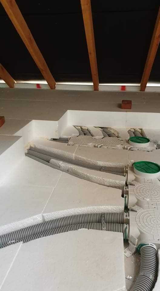 Montaż instalacji podłogowej z rurkami w izolacji, widoczne drewniane elementy konstrukcji dachu.