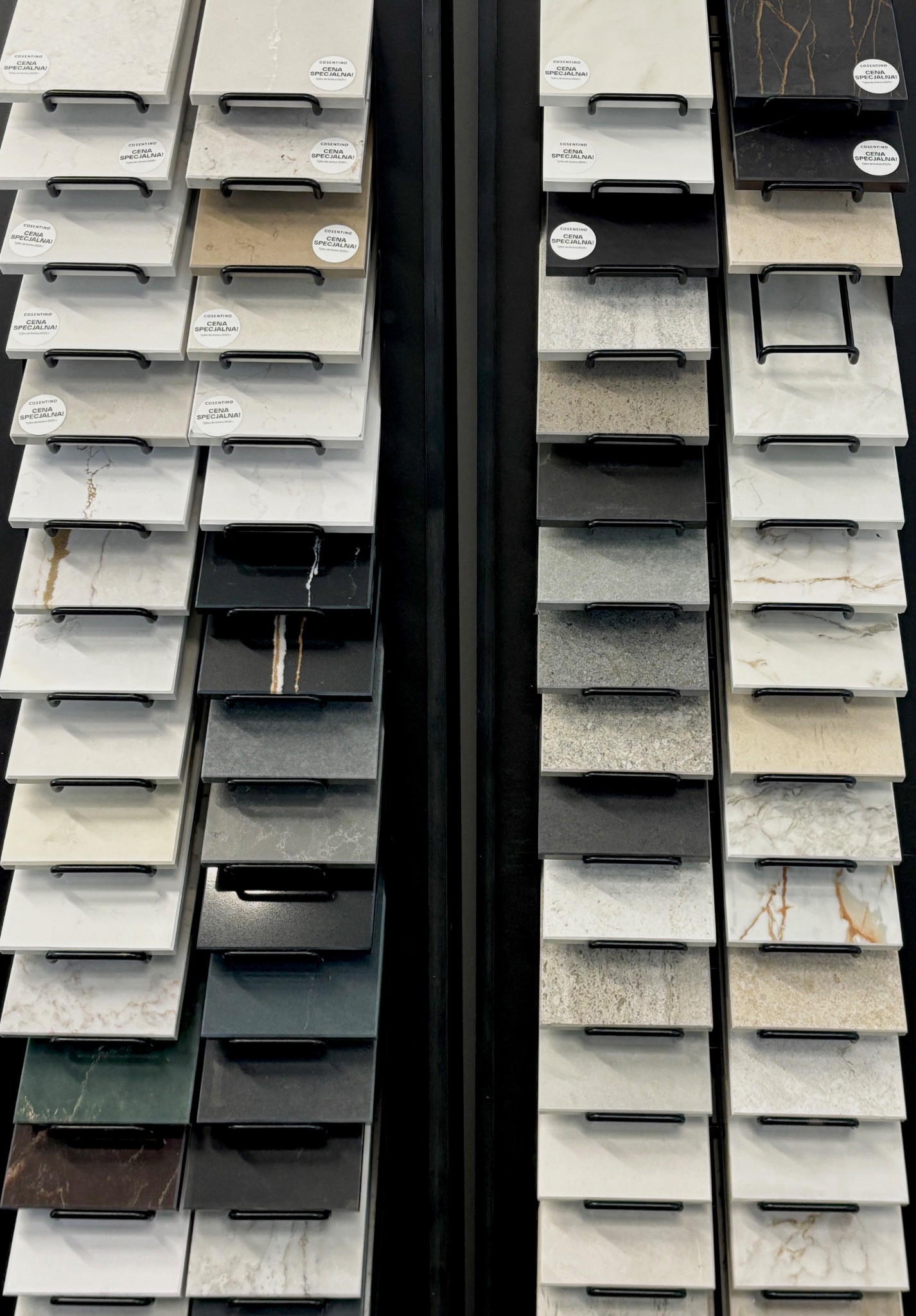 Ekspozycja próbek materiałów wykończeniowych, w tym płytek i kamieni, ułożonych na metalowych stojakach z etykietami 'Cena Specjalna!'.