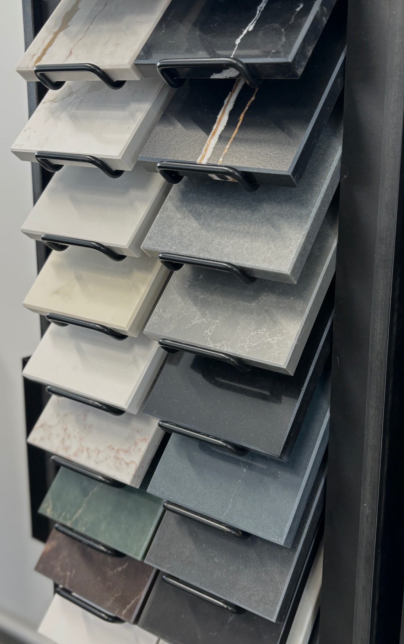 Ekspozycja próbek blatów kuchennych z różnego rodzaju kamienia, w tym marmuru, granitu i kwarcu, umieszczonych na metalowym stojaku w salonie wystawowym.