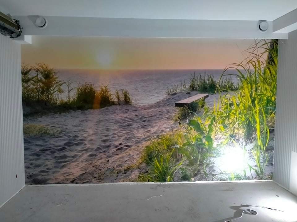 Fototapeta z motywem plaży i zachodzącego słońca, naklejona na ścianie w jasnym pokoju, widoczne niedoskonałości na łączeniach tapety.