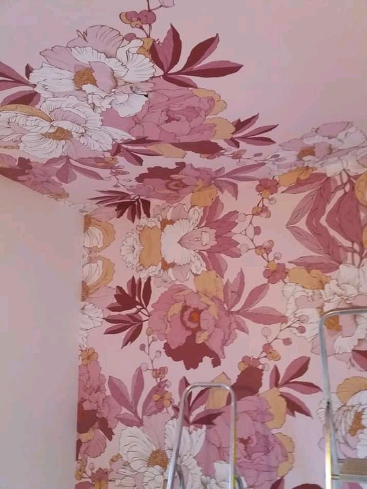 Różowe i białe kwiatowe tapety pokrywają ściany i sufit, drabina w rogu pokoju.