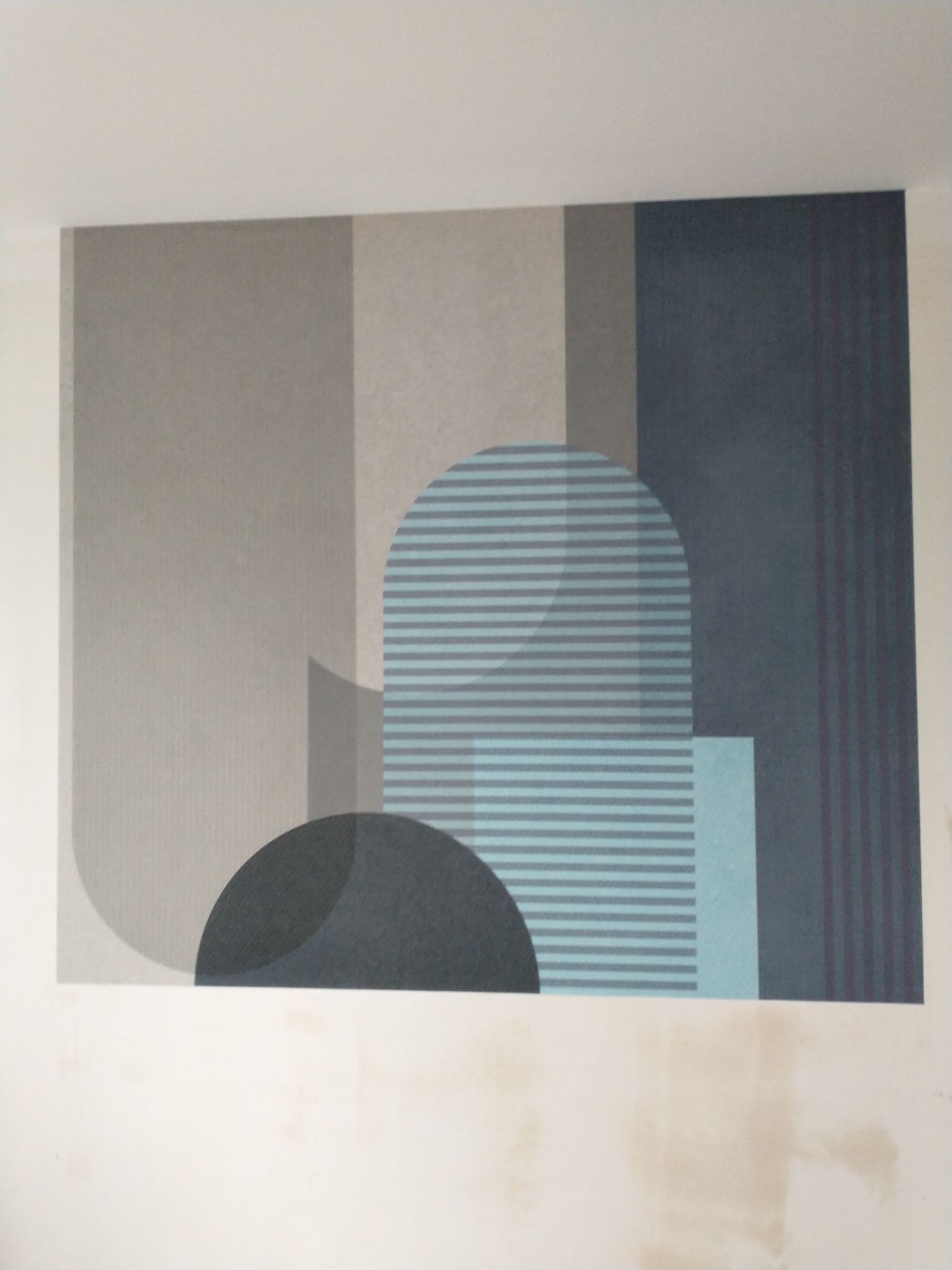 Geometryczny wzór tapety w odcieniach szarości i błękitu, z widocznymi niedoskonałościami ściany u dołu.