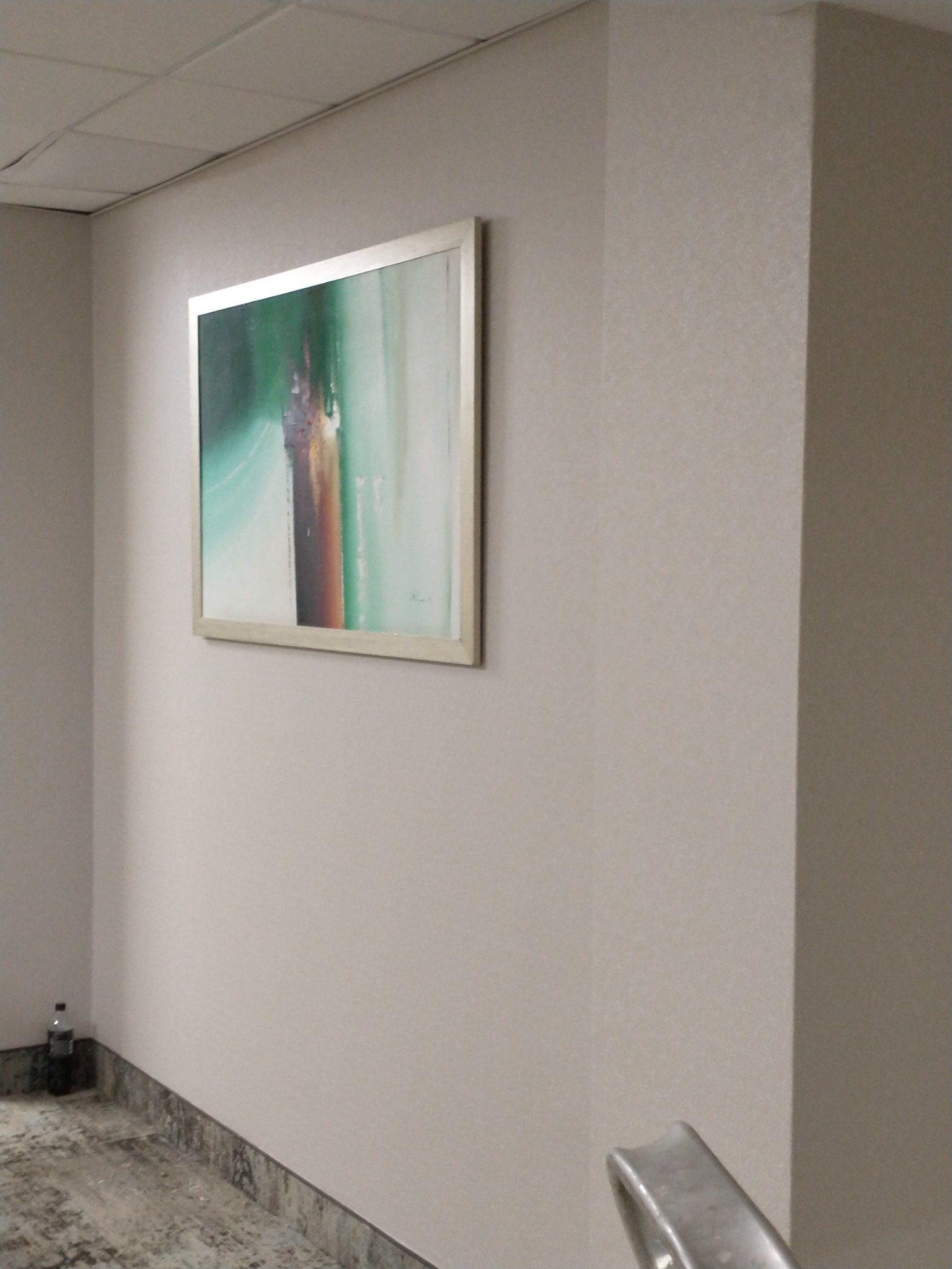 Ściana w biurze pokryta tapetą o delikatnej strukturze, na ścianie wisi obraz w ramie, widoczny fragment schodów.