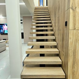 POLMAKS Schody Szyte Ogniem - Drewniane schody wspornikowe z czarnymi elementami w nowoczesnym wnętrzu domu w Kleosinie. Ściana wykończona panelami drewnopodobnymi.
