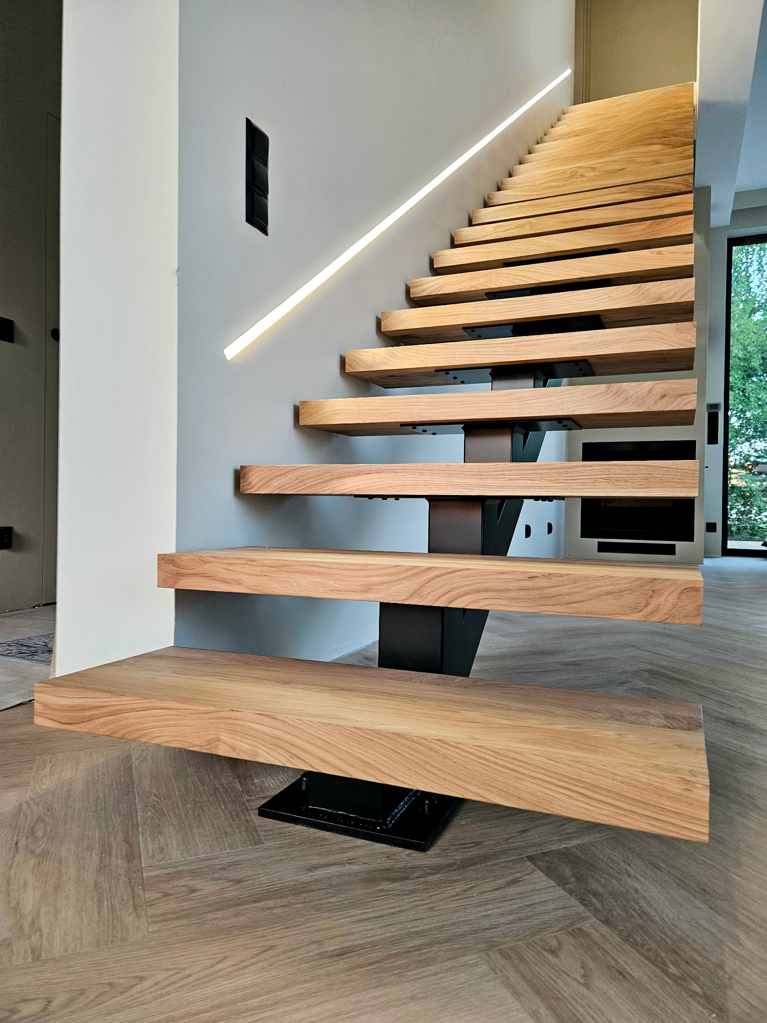 Nowoczesne, drewniane schody wspornikowe z podświetleniem LED wzdłuż ściany, wykonane w Kleosinie, z widoczną strukturą drewna i czarnymi elementami mocującymi.