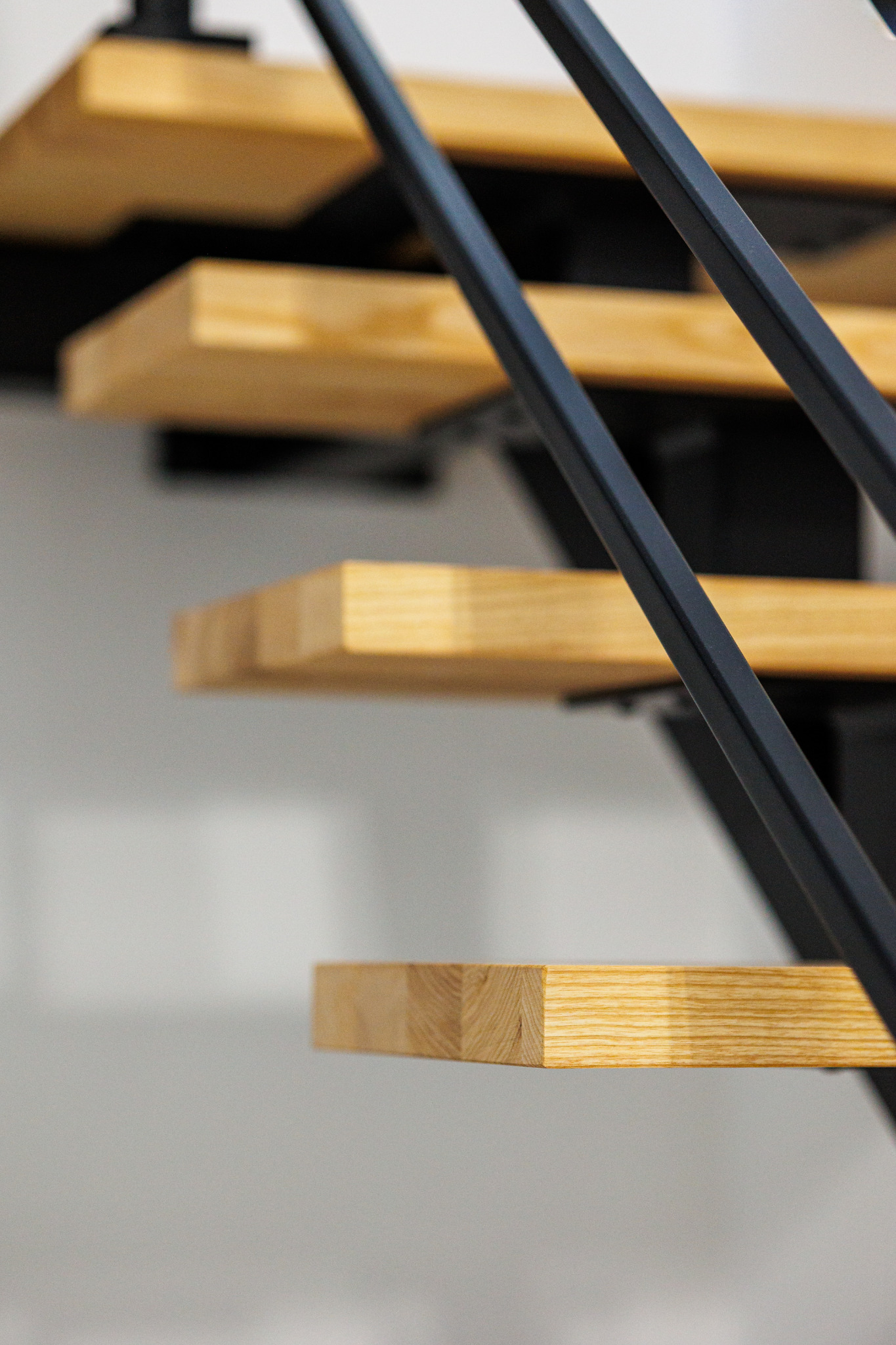 Nowoczesne schody z drewnianymi stopniami i metalową balustradą w kolorze grafitowym, widok z dołu, jasne tło.