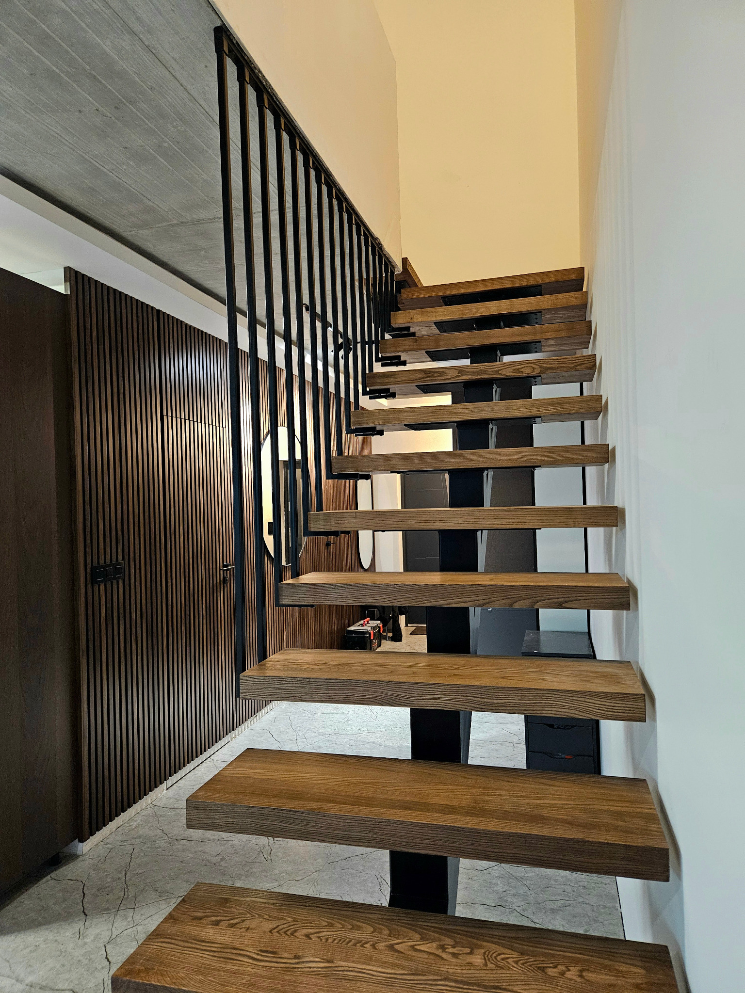 Nowoczesne schody z drewnianymi stopniami i czarną metalową balustradą, widok z dołu, z elementami dekoracyjnymi na ścianie w tle.