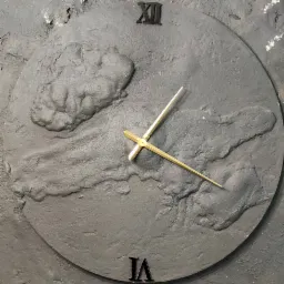 Dekoracyjny zegar ścienny z szarego tynku strukturalnego z wypukłymi elementami i złotymi wskazówkami, wskazujący godzinę.