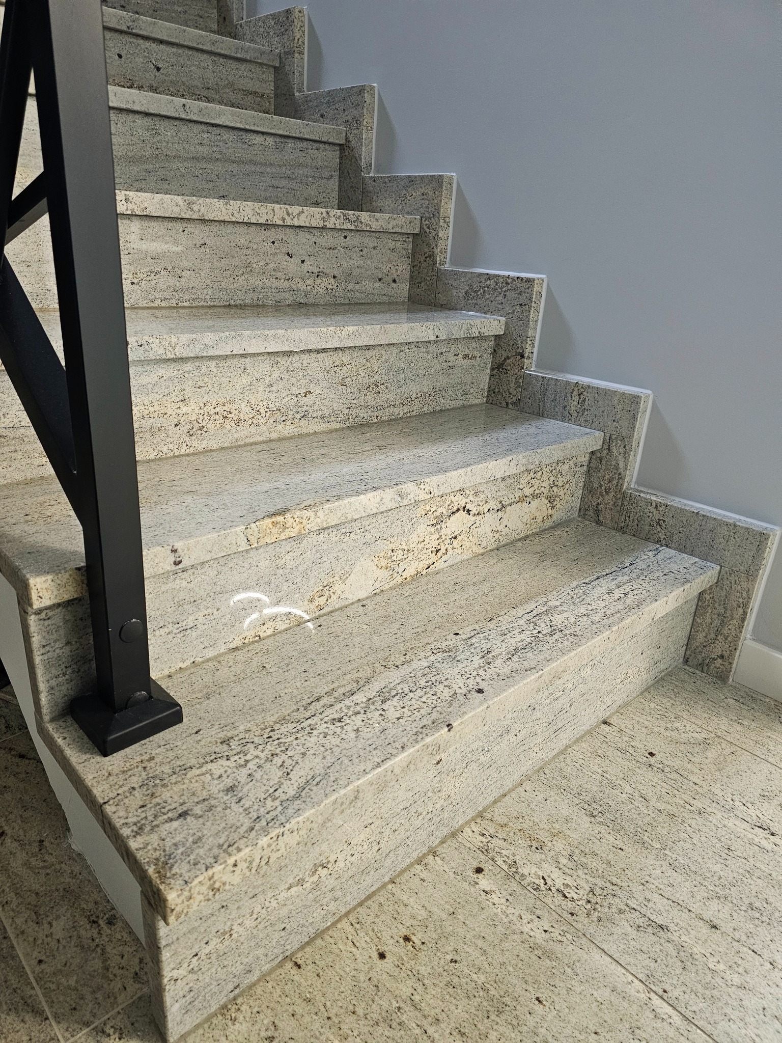 Granitowe schody wewnętrzne z czarną, metalową balustradą, widok z dołu ukazujący strukturę kamienia i detale wykończenia.