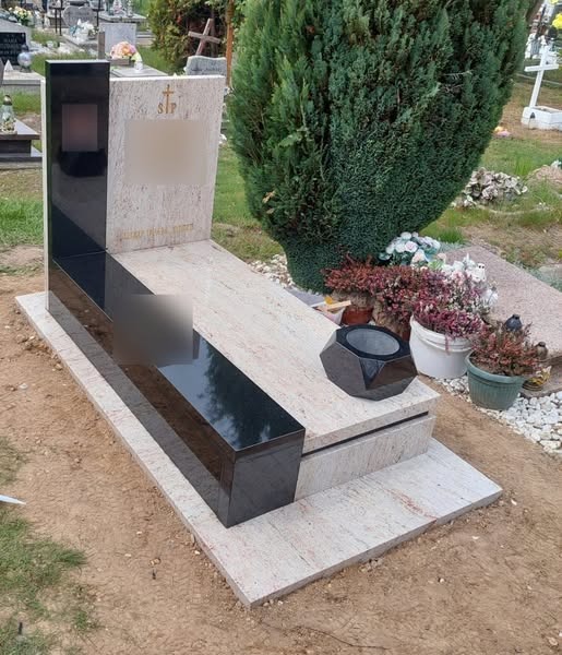 Jasny, granitowy pomnik z czarnymi, błyszczącymi elementami, ozdobiony geometryczną wazą na kwiaty, ustawiony na cmentarzu z widoczną zielenią drzew i innymi nagrobkami w tle.