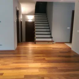 Wnętrze domu po ułożeniu parkietu z egzotycznego drewna w odcieniach brązu, widoczne schody i instalacja elektryczna wymagająca wykończenia.