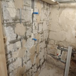 Damian Kołodziej - Ściana z fragmentami starego tynku, przygotowana pod gładź, z widocznymi instalacjami wodnymi i elementami konstrukcji sufitu podwieszanego.