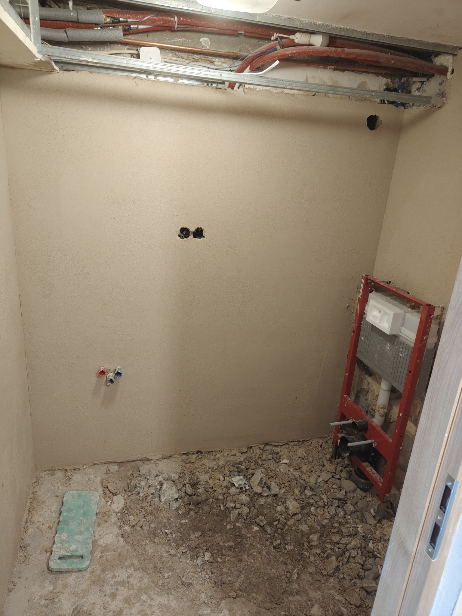 Remont łazienki w trakcie: widoczne instalacje podtynkowe, rury, stelaż WC, ściany po szpachlowaniu, gruz na podłodze. Etap przygotowania do wykończenia.