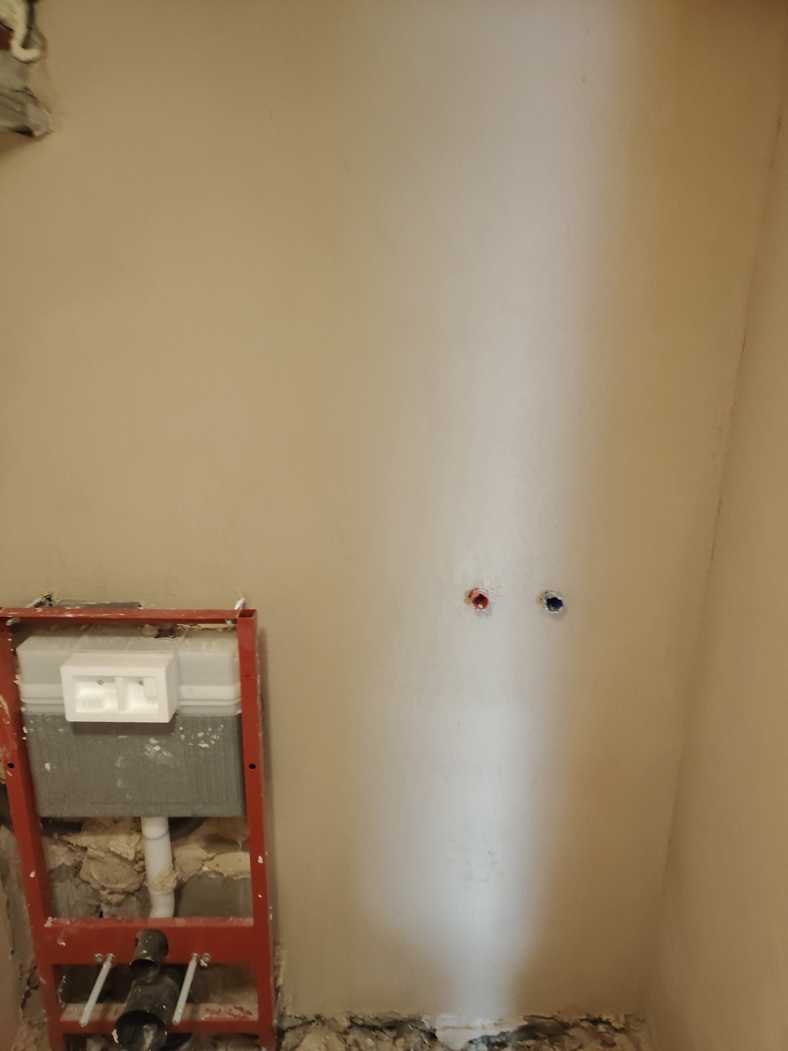 Ściana w trakcie remontu łazienki z zamontowanym stelażem podtynkowym WC i wyprowadzonymi przyłączami wodnymi. Widoczne ślady po kuciu i przygotowaniu podłoża.