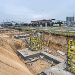 Fundamenty pod budowę hali, szalunki Doka Frami Xlife, wykop ziemny, widok na teren budowy z elementami infrastruktury miejskiej w tle.