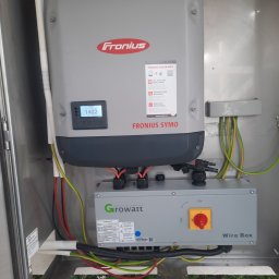 Bogdan Topolanek - Szara skrzynka z falownikiem Fronius Symo i Growatt Wire Box w metalowej obudowie, widoczne kable elektryczne w kolorach czerwonym, zielonym i żółtym, wyświetlacz LCD pokazuje wartość 1402.
