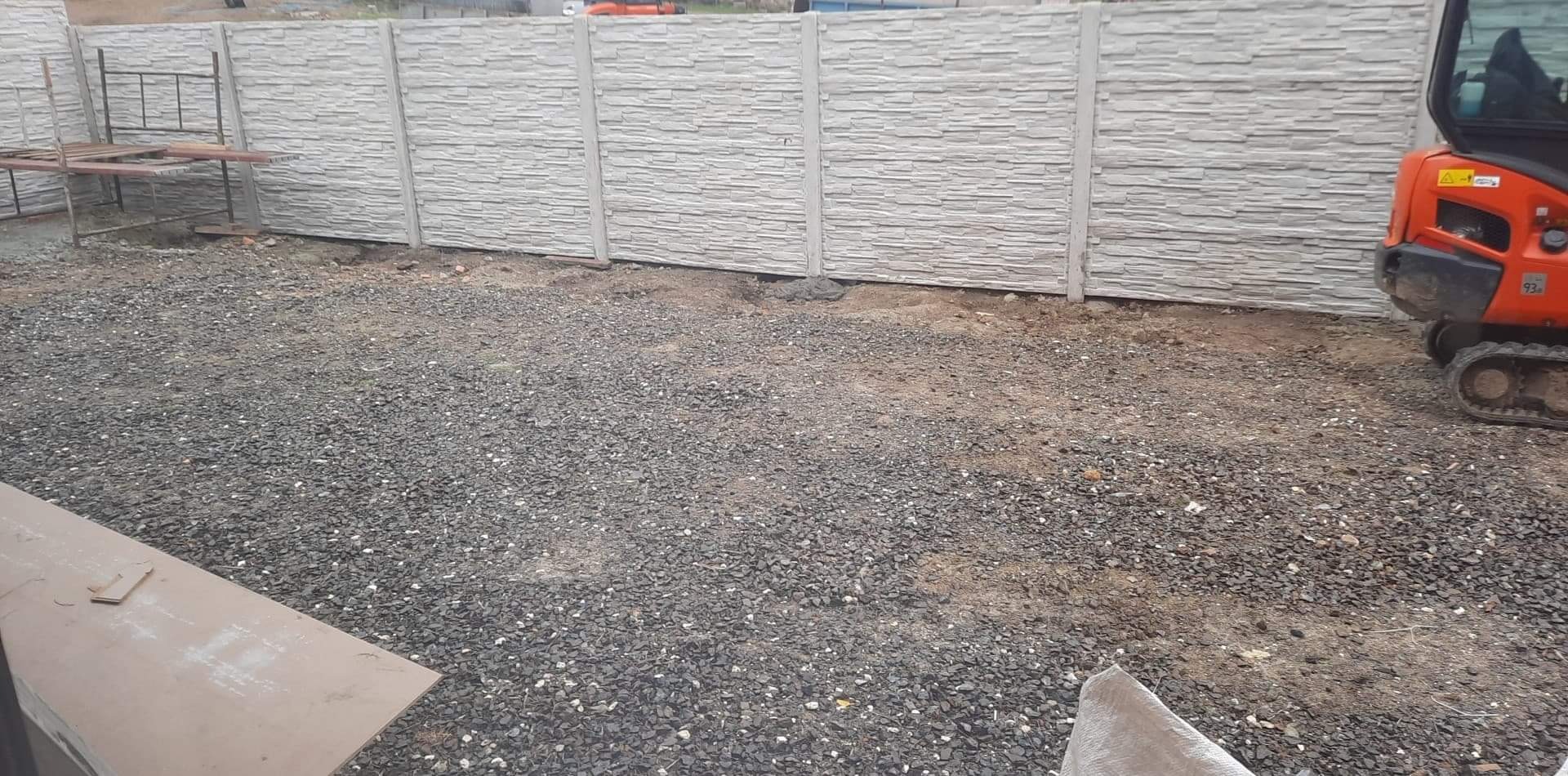 Montaż prefabrykowanego ogrodzenia betonowego z użyciem mini koparki, teren przygotowany pod dalsze prace ziemne, widoczne płyty z fakturą kamienia.