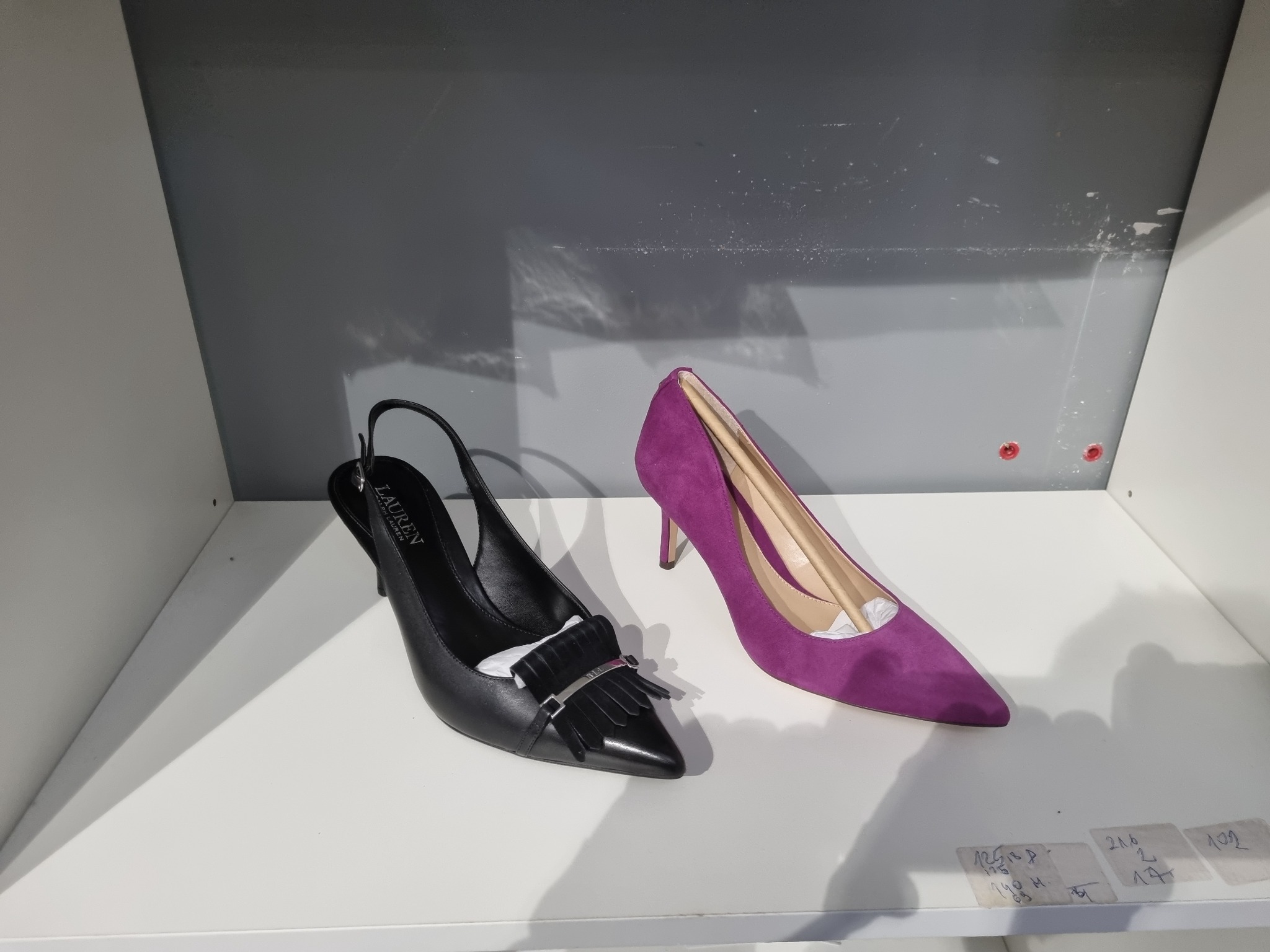 Para szpilek: czarne skórzane z frędzlami marki Lauren i fioletowe zamszowe na białej półce.