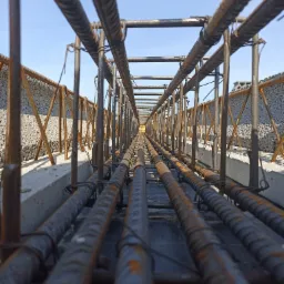 Zbrojenie fundamentów z widocznymi prętami żebrowanymi połączonymi drutem, krawędź betonowa i bloczki betonowe w tle, perspektywa z dołu do góry.