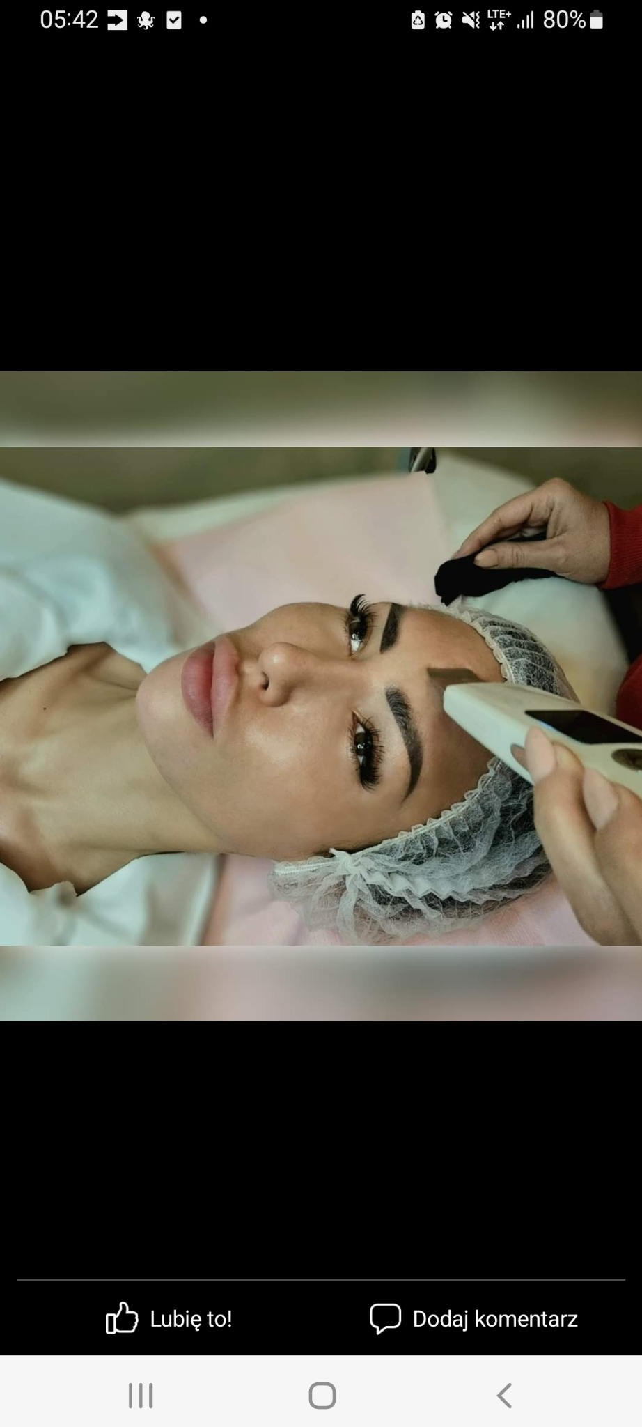 Klientka w czepku ochronnym leży na leżance, podczas zabiegu pilingu kawitacyjnego na brwiach wykonywanego przez kosmetyczkę przy użyciu urządzenia z białą głowicą.